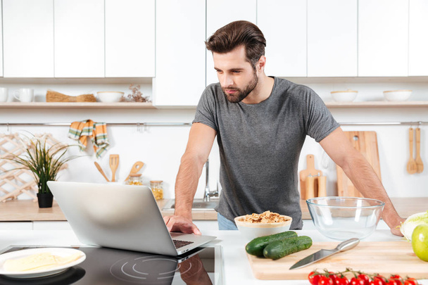 Man looking recipe on laptop in kitchen at home - Foto, Imagen