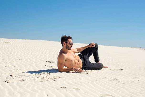 Un joven guapo luce un físico tumbado en la arena
 - Foto, imagen