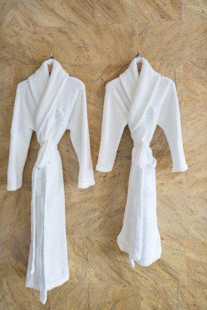 Het beeld van een paar witte badjassen op een hanger in badkamer. - Foto, afbeelding