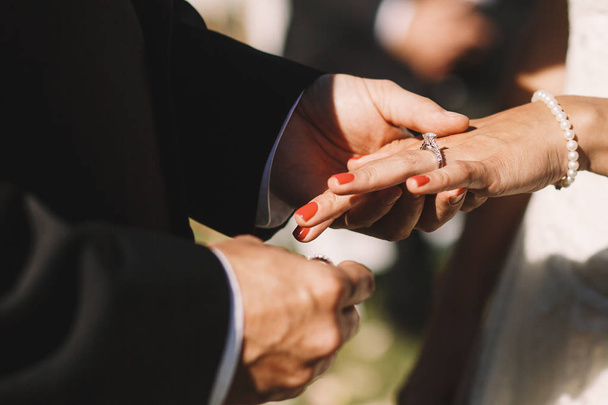 Groom puts a wedding ring over bride's finger holding it tender - Foto, afbeelding