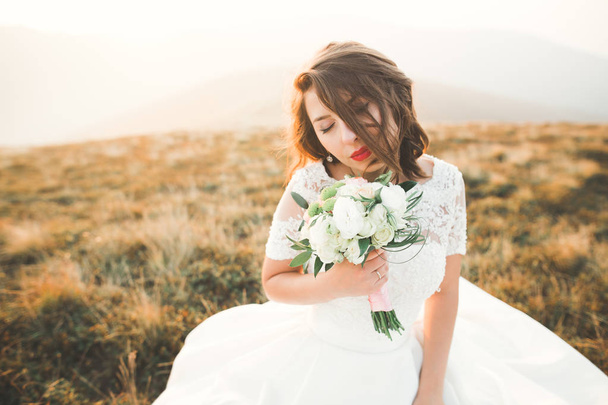 Beautiful bride with a bouquet on mountain background at sunset - Fotoğraf, Görsel
