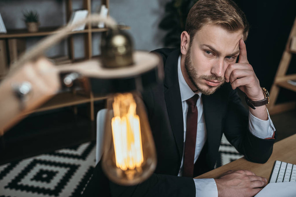 businessman looking at lamp while sitting at workplace - Фото, изображение