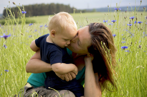Bonne famille dans le domaine des fleurs soufflées. Belle jeune mère embrasse son adorable petit garçon. Concept de bonheur
 - Photo, image