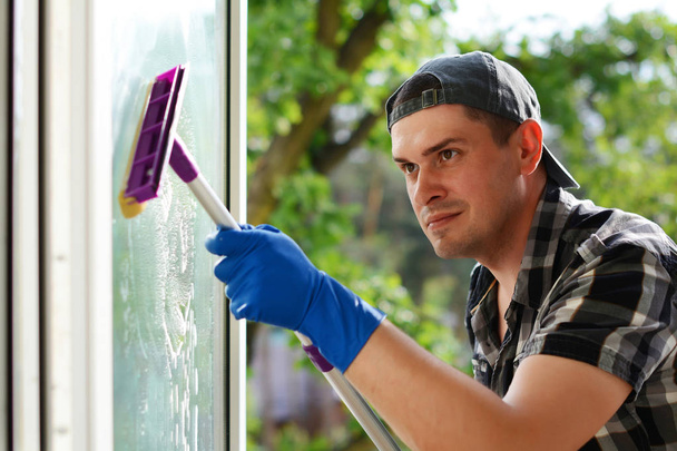 Jeune homme nettoyant la fenêtre avec une serpillière. Lave-vitre. Entreprise de nettoyage professionnelle
. - Photo, image