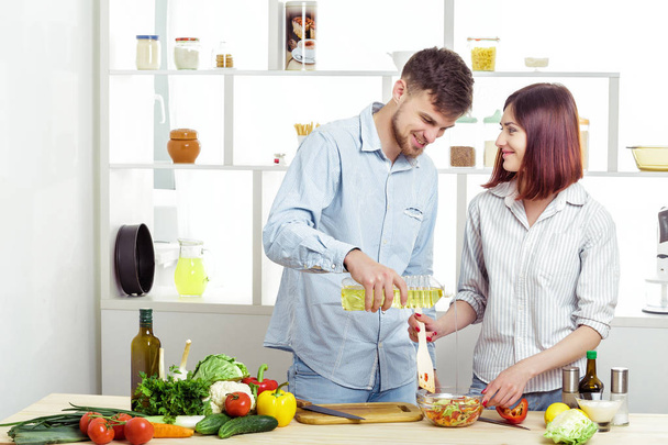 Loving happy couple preparing healthy salad of fresh vegetables in kitchen - Фото, изображение