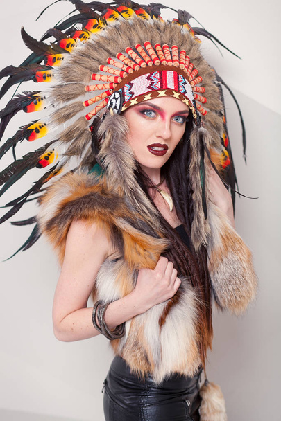Indianerin mit traditionellem Make-up und Kopfbedeckung, die in die Kamera blickt. Rothaut-Indianerin auf weißem Hintergrund mit einer Kakerlake auf dem Kopf - Foto, Bild