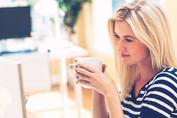 Young woman drinking coffee in an office - Foto, imagen