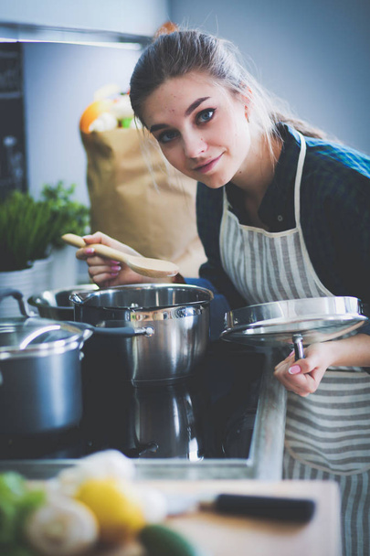 Young woman standing by the stove in the kitchen . - Фото, изображение