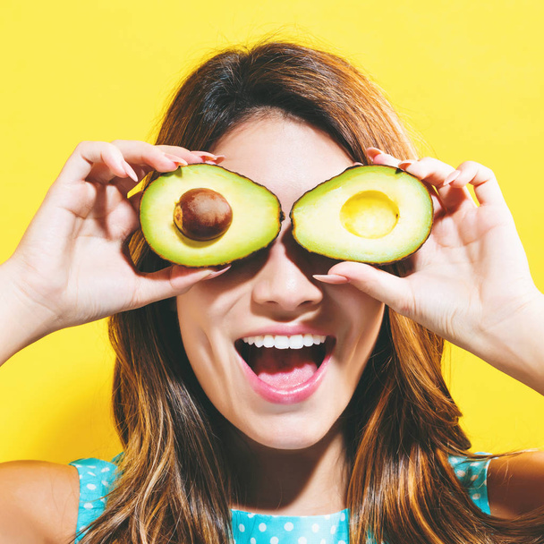 Happy young woman holding avocado halves - Фото, изображение