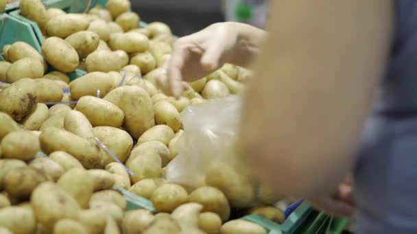 Female hands put ripe potatoes in the transparent plastic packing bag. Woman chooses ripe potatoes adds to the package. Shopping and people concept. Stock video footage. - Video, Çekim