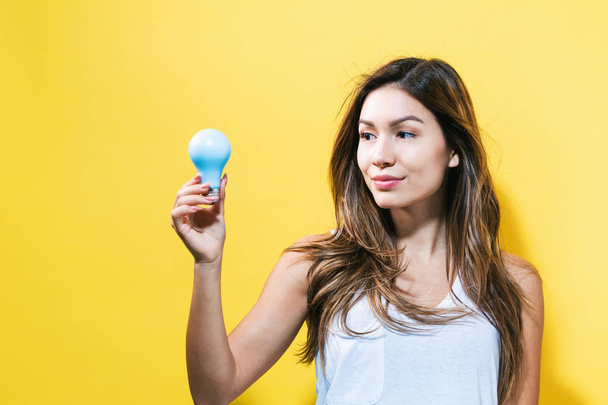 Young woman holding a light bulb - Фото, изображение