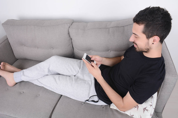 Man using smartphone on couch. - Foto, afbeelding