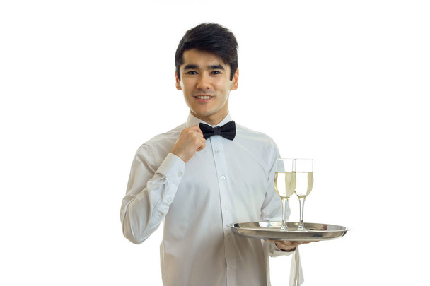 charming young waiter in a beautiful dress looks straight and holding a tray with glasses - Фото, изображение