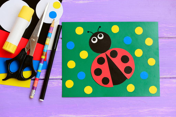 Bright ladybug cardboard card. Green card with ladybug, scissors, glue stick, pencil, marker, cardboard set on a wooden table. Summer homemade card idea to make. Closeup - Photo, Image