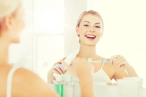 woman with toothbrush cleaning teeth at bathroom - Photo, image