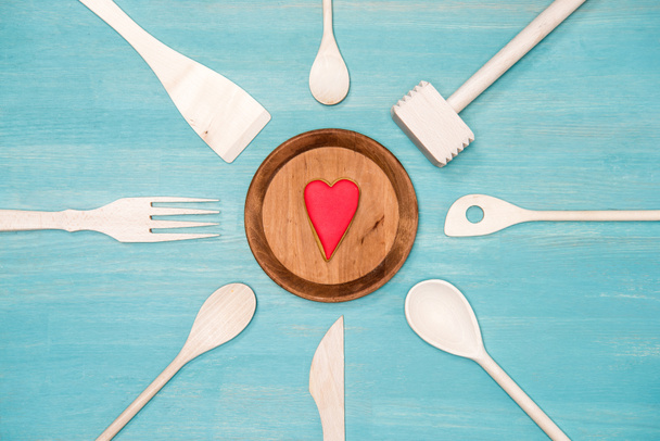 Draufsicht auf verschiedene Kochutensilien aus Holz mit Herzsymbol auf dem Teller - Foto, Bild