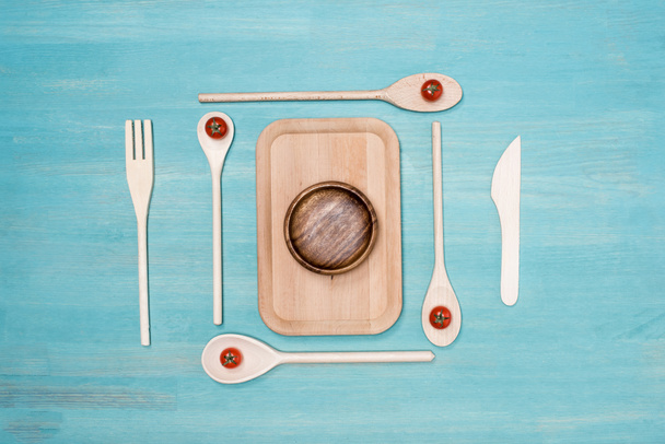 Bovenaanzicht van houten snijplank met keukengerei en cherry tomaten op tafel - Foto, afbeelding