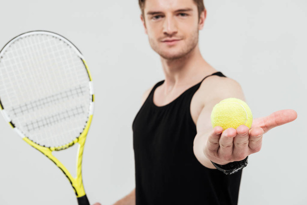 Pohledný mladý sportovec drží tenisák a raketa - Fotografie, Obrázek