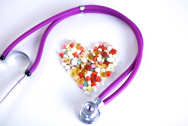 Zblízka pilulek rozloženo v tabulce s stetoskop a srdcem ležící vedle - Fotografie, Obrázek