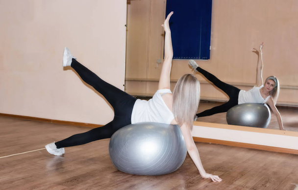 Изысканная молодая девушка делает упражнения на мяче для упражнений
 - Фото, изображение