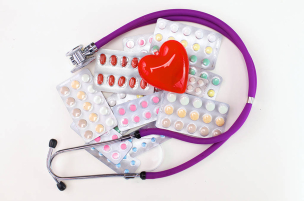 Gros plan des pilules réparties sur la table avec stéthoscope et cœur couché à côté
 - Photo, image