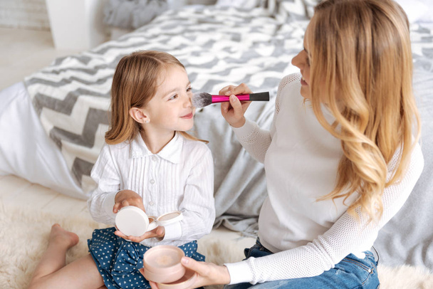 Cheerful mother applying powder to her daughters nose - Photo, Image