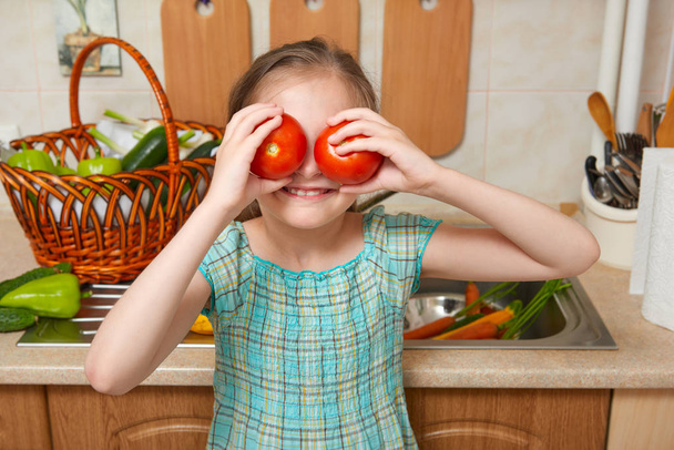 child girl with tomatoes, vegetables and fresh fruits in kitchen interior, healthy food concept - Photo, Image