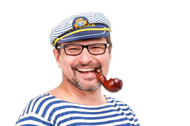 A man sailor in a cap with a smoking pipe in front of a white ba - Foto, afbeelding