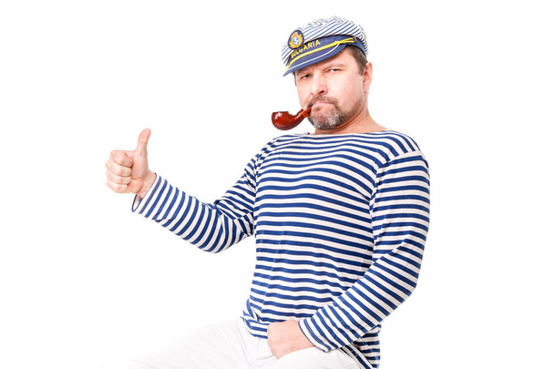 Un marinero con gorra y pipa humeante delante de una ba blanca
 - Foto, Imagen