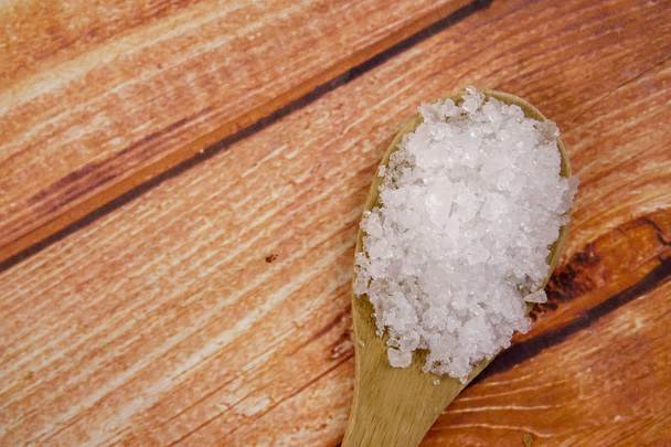 Морская соль в деревянной ложке. Также называется лавровой солью или солнечной солью, используется в кулинарии и косметике. Грубые зернистые кристаллы минерала
. - Фото, изображение