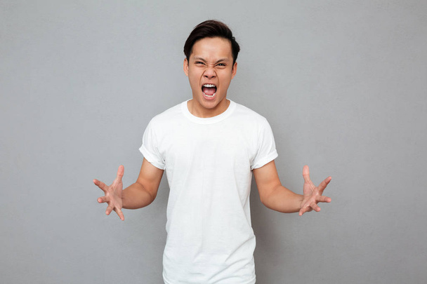 Screaming young asian man standing over grey background - Photo, Image