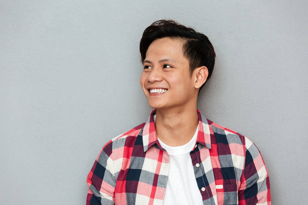 Young smiling asian man standing over grey wall. - Φωτογραφία, εικόνα
