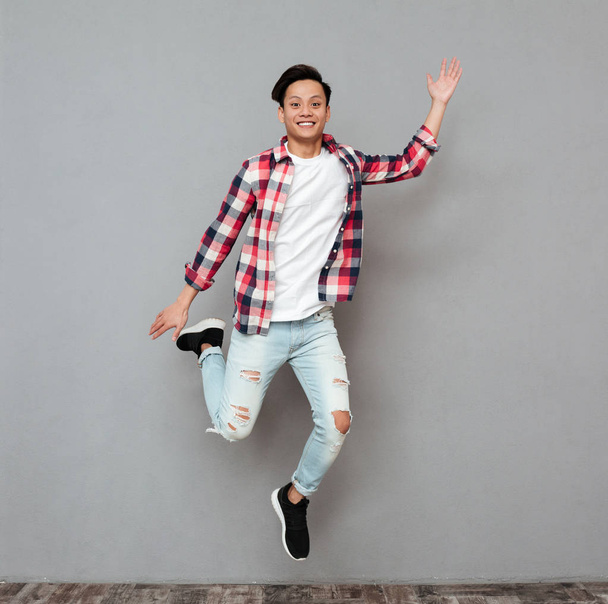 Jumping young asian man over grey background. - Fotografie, Obrázek