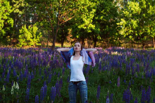Mulher jovem esbelta bonita (menina) contra o fundo de uma clareira com flores roxas. O conceito de sair no verão na natureza. Retrato na anca. Luz do dia, tiro ao ar livre
 - Foto, Imagem