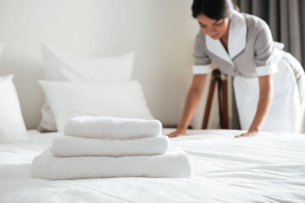Young hotel maid setting up pillow on bed - Foto, afbeelding