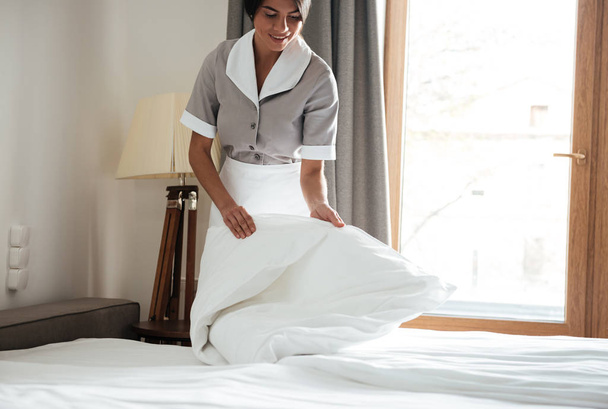 Maid setting up white bed sheet in hotel room - 写真・画像