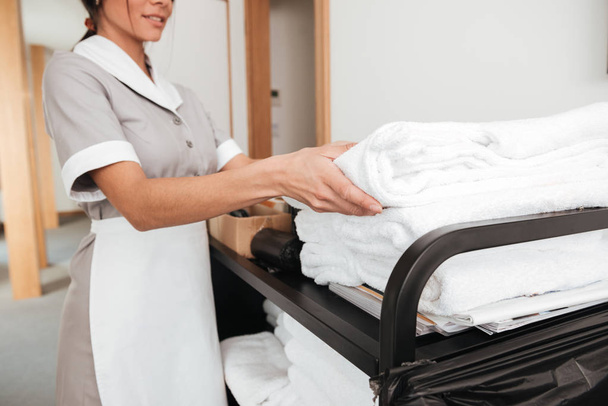 Smiling young maid taking fresh towels from a housekeeping cart - Photo, Image
