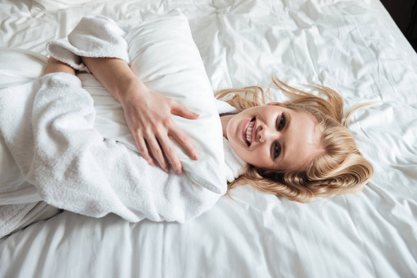 Happy young woman in bathrobe lying on bed - Zdjęcie, obraz