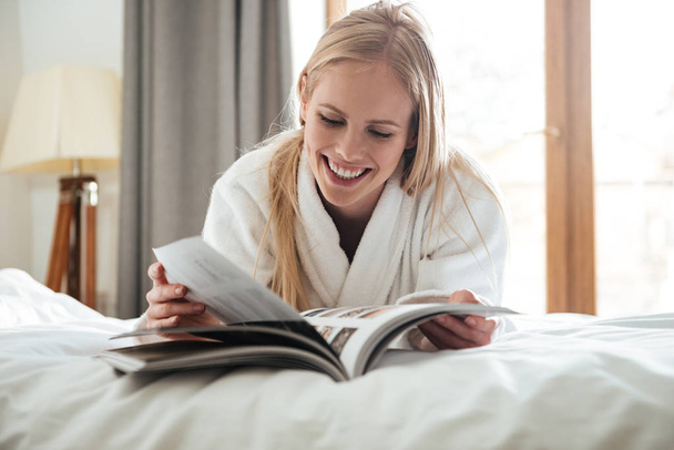 Młoda Blondynka czytania magazynu leżąc na łóżku - Zdjęcie, obraz