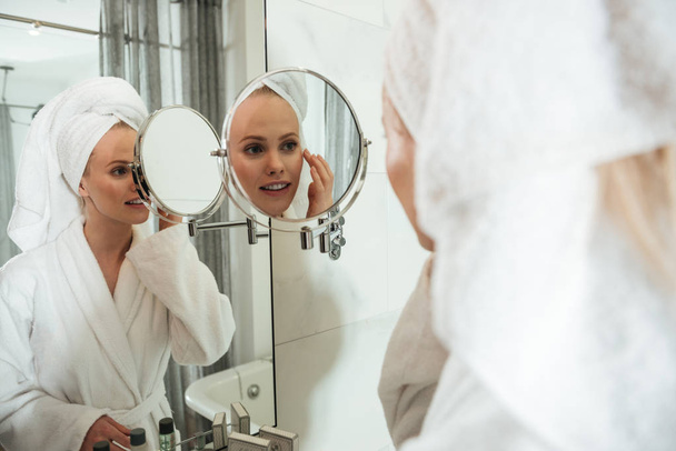 Young blonde woman looking in mirror to apply cosmetics - Foto, afbeelding