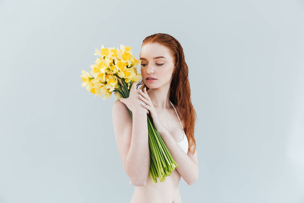 Fashion portrait of a young redheaded woman holding narcisuss flowers - Fotó, kép