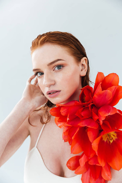 Close up portrait of a redheaded woman holding tulip flowers - 写真・画像