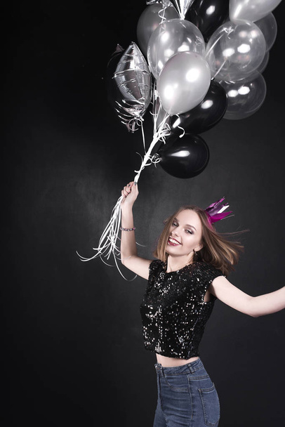 Close up fashion portrait of a young beautiful elegant girl with bright party make up in evening black sequin top. She is keeping silver stars balloons in her hand. Girl at the party. Retouched shot - Фото, изображение