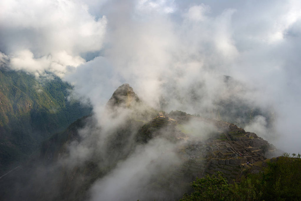 Machu Picchu illuminated by the first sunlight coming out from the opening clouds. The Inca's city is the most visited travel destination in Peru. Mist, clouds and fog covering the valley. - Photo, Image