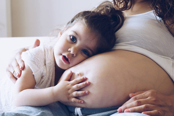 Ευτυχισμένο παιδί κορίτσι αγκαλιάζει έγκυος μητέρα κοιλιά - Φωτογραφία, εικόνα