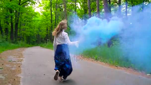 Nainen kauniissa vaatteissa kulkee metsän läpi heiluttaen värillistä savua
 - Materiaali, video