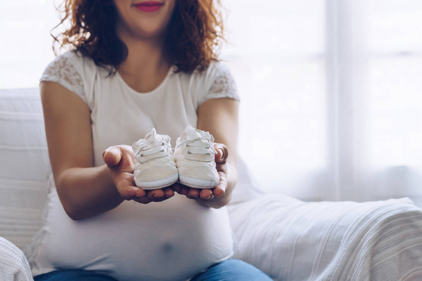 Mujer embarazada feliz sosteniendo zapatos de bebé en sus manos
 - Foto, Imagen