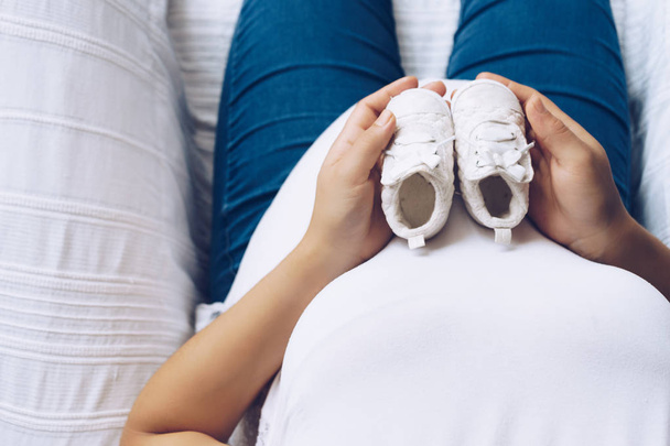 Femme enceinte tenant des chaussures de bébé dans ses mains, vue du dessus
 - Photo, image