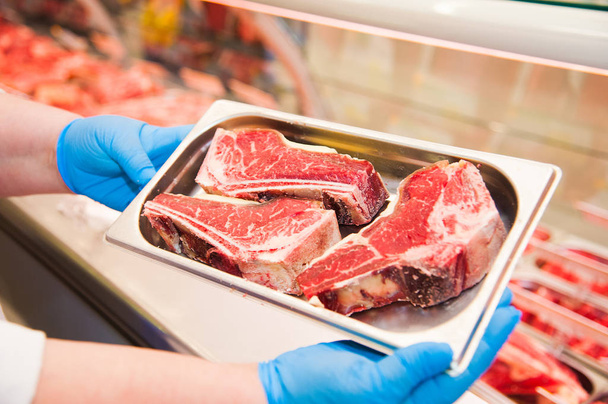 Close-up de mãos de açougueiro segurando pedaço de carne na loja
 - Foto, Imagem