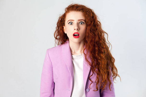 Portrait of shocked beautiful business woman with red - brown hair and makeup in pink suit. looking at camera, studio shot on gray background. - Фото, изображение
